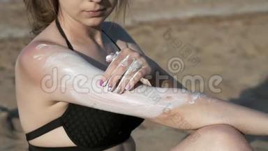 穿着黑色泳衣的海滩上的女孩涂了<strong>防晒</strong>霜或<strong>防晒</strong>霜。 在海边的沙滩上